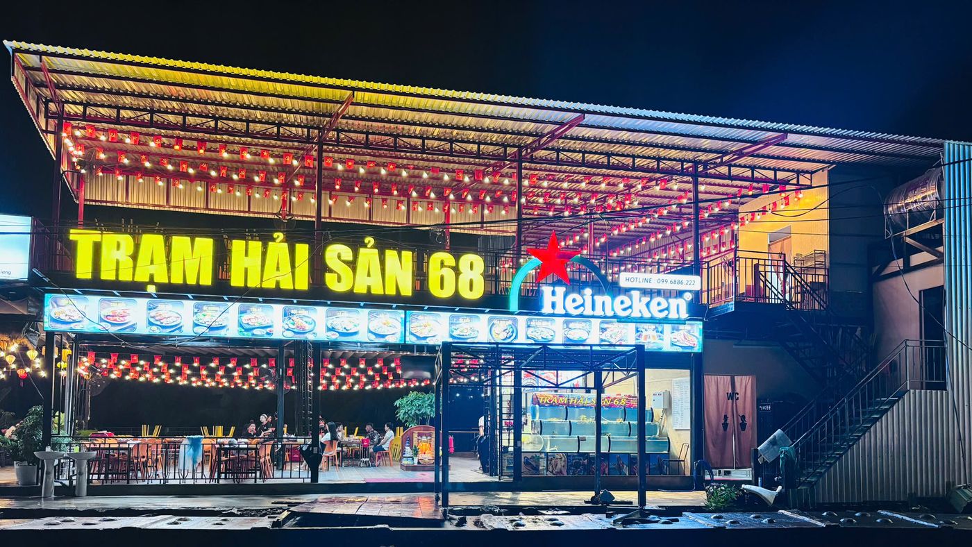 Mặt tiền Trạm Hải Sản 68 lên đèn buổi tối, biển hiệu chữ vàng lớn, bể hải sản sống phía trước